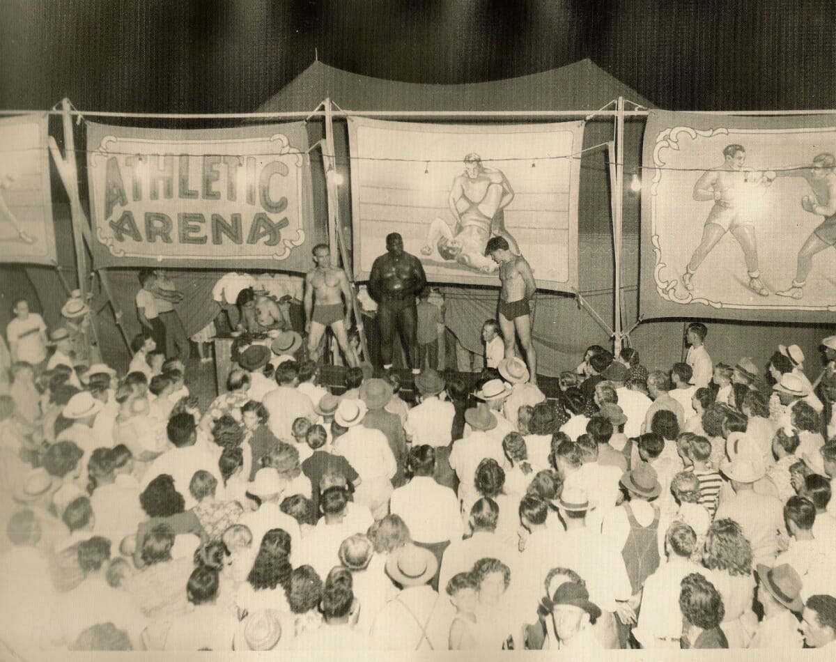 A crowd gathered around a carnival wrestling arena
